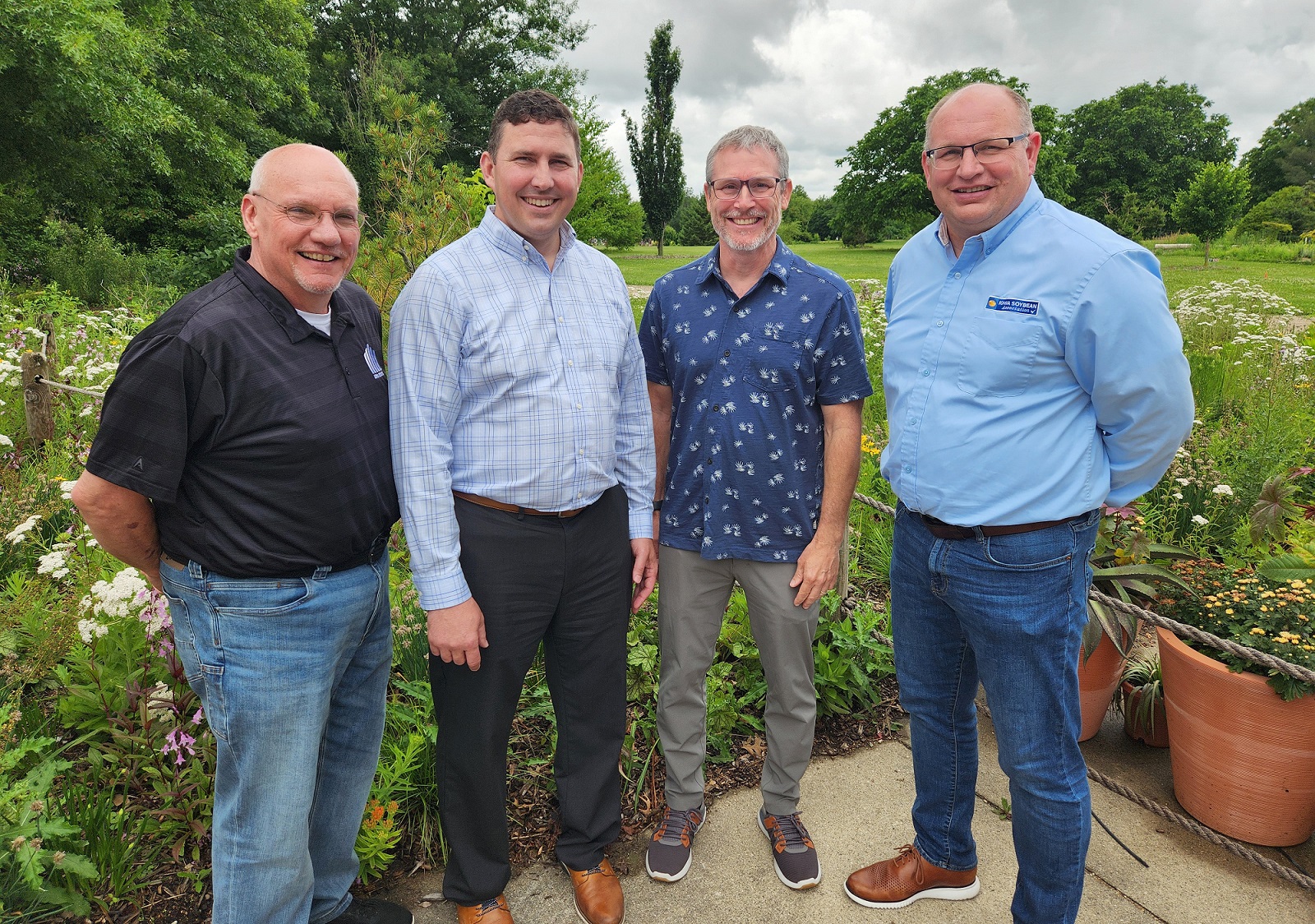 Four men stand side by side in a garden smiling.