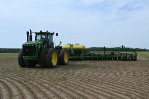 A large green tractor is attached to a large airseeder planter in a field.