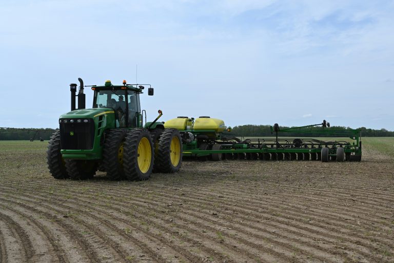 A large green tractor is attached to a large airseeder planter in a field.